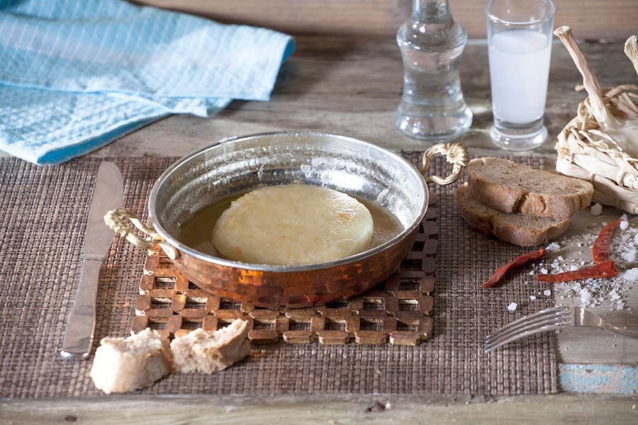 pan with 'Mystakelli Dairy ' white cheese in oil and pieces of dry bread and glass of ouzo